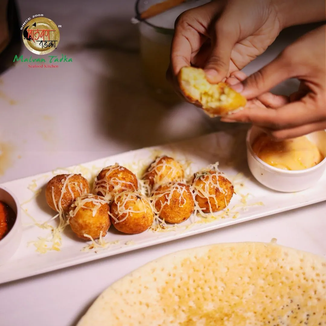 Hands breaking open cheese-topped fried snacks beside a ghavan