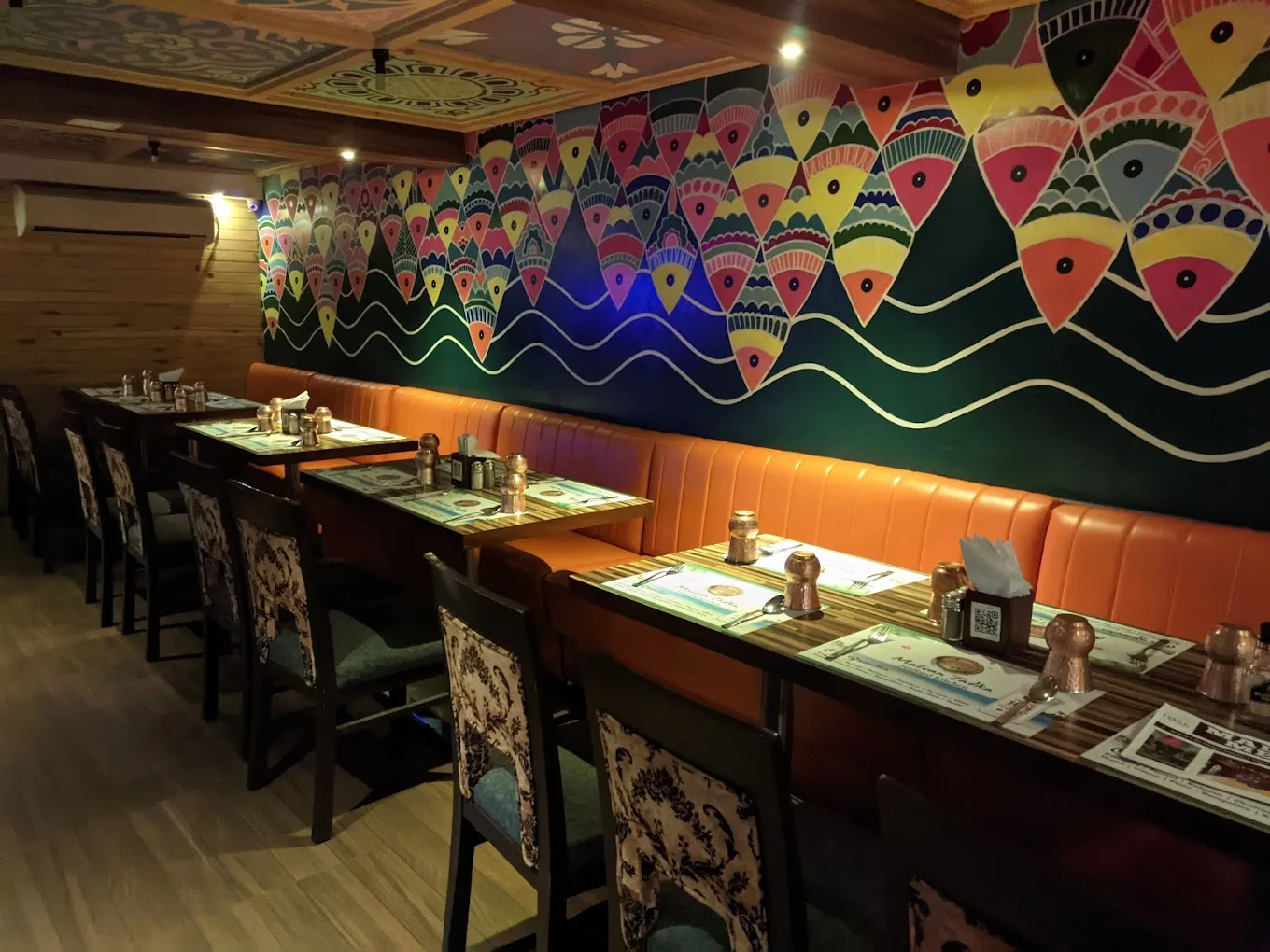 Warli-style fish mural above orange banquettes