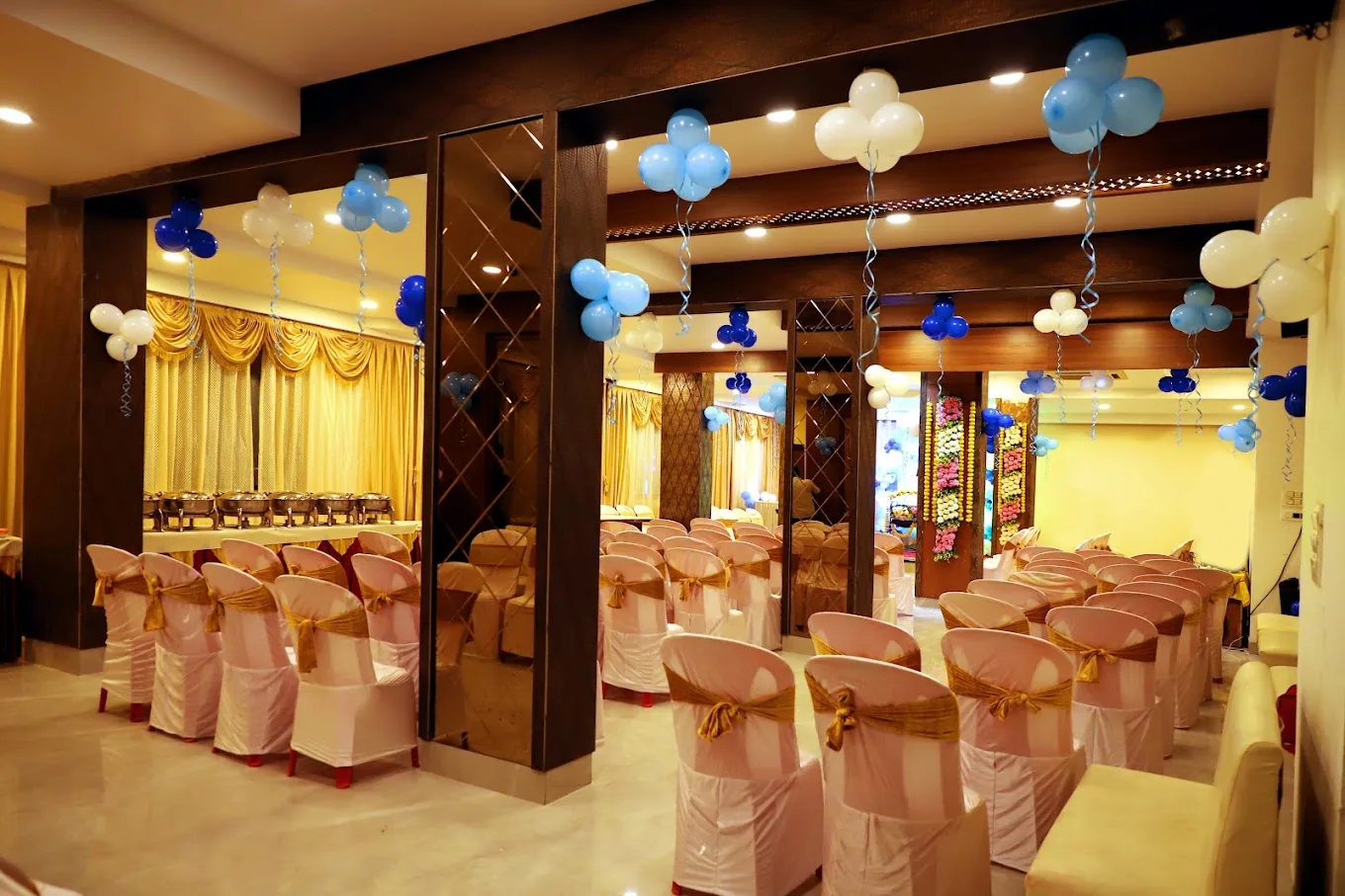 A banquet hall with gold-sashed chairs and balloons